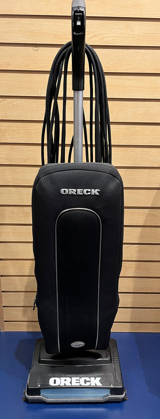 A Sew & Vac Oreck XL21 upright vacuum cleaner, certified reconditioned for everyday cleaning, with a black fabric bag and a silver handle against a wooden slat background.