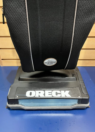 Close-up of a Certified Reconditioned Sew & Vac Oreck XL21 vacuum cleaner, ideal for everyday cleaning, on a blue surface with a wooden background.