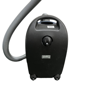 A black, wheeled Miele C3 Marin vacuum cleaner from Sew & Vac, certified refurbished with a flexible hose attached. The handle is on top, and there is a label on the front of the unit.