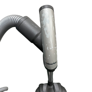 Close-up of a certified refurbished vacuum cleaner hose with visible wear and peeling paint on the handle, showcasing the brand name "Sew & Vac," alongside Miele C3 Marin bags and filters.