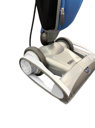 Close-up of the base of an Oreck Magnesium upright vacuum by Imagine Sewing & Vacuum, silver and blue, showing its wheels and part of the dust bag.