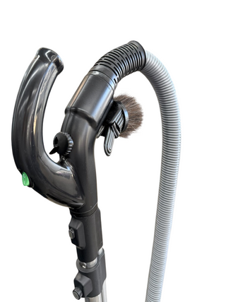 A close-up of the Simplicity Wonder canister vacuum handle by Imagine Sewing & Vacuum, featuring a gray flexible hose and round brush accessory, isolated on a white background.