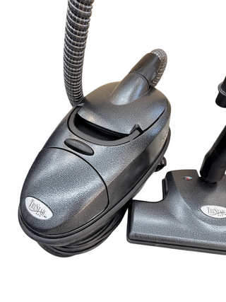 A refurbished gray TriStar CS Canister vacuum from Imagine Sewing & Vacuum, featuring powerful suction, a hose attachment, and floor nozzle, is displayed against a white background.