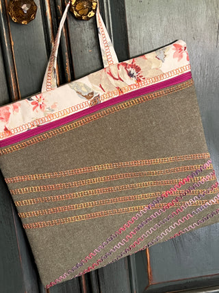 A decorative cloth tote bag, crafted with multicolored stitching patterns from the Sew & Vac Baby Lock Applaud Creative Coverstitch & Serger Extravaganza, is hanging on a wooden door by its handles.