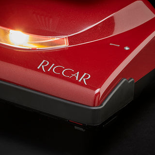 Close-up of a Riccar R10P Lightweight Supralite Premium upright vacuum cleaner in red, featuring an illuminated light on the front.