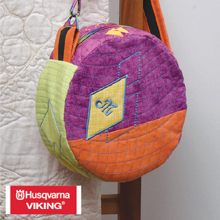 The Ravish Me 'Round Bag, created with patchwork-in-the-hoop in vibrant colors, hangs on a hook. Join the South Jordan In-Store Class for this 2-day event on November 5-6, 10–5 pm.