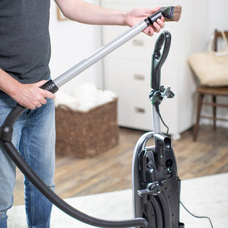 A man using a Tandem Air Deluxe Upright Vacuum Anniversary Model by 10-Tacony with HEPA media filtration in a living room.