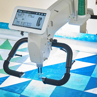 A Quilter's Academy - Soph from Sew & Vac, featuring a digital screen and handlebars, is stitching a blue and white triangular quilt pattern, making it perfect for students enrolled in Quilter's Academy or anyone taking a beginner quilting class.