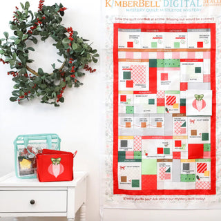 The Kimberbell 2026 DDE Embroidery Club Mystery Quilt: Mistletoe Mystery by 42-Kimberbell, a Christmas-themed quilt made with machine embroidery, hangs between a red-berry wreath and shelves filled with colorful sprays and sewing supplies.