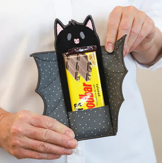 A person holds an open, bat-shaped fabric pouch—perfect for Halloween embroidery—made at the Kimberbell "The Stitching Hour" 2-Day Event (Layton In-Store Class, Aug 14-15, 2026).