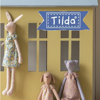 Three handmade dolls—two rabbits and a cat in floral dresses—are displayed with a blue "Tilda" sign, showcasing the charm of Tilda Dolls from 1000-Education’s Tilda Club & Friends, held every 3rd Thursday of each month.