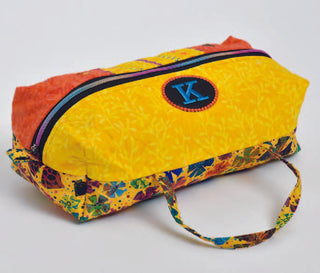 The Sew & Vac Viking Husqvarna Treasure Tote from the Embroidery Event features a vibrant yellow and red floral pattern on colorful fabric with a handle. It includes a round patch with a blue "K," crafted using the DESIGNER EPIC 3, and has a convenient zippered closure.