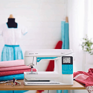 A Husqvarna Viking sewing machine sits on a table next to some fabric.