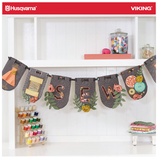 A "SEW" fabric banner with sewing supplies and Husqvarna Viking jars inspires creativity—perfect for the Layton In-Store Class: HANGIN' BY A THREAD Husqvarna Viking 2-day Event, June 26–27, 2026.
