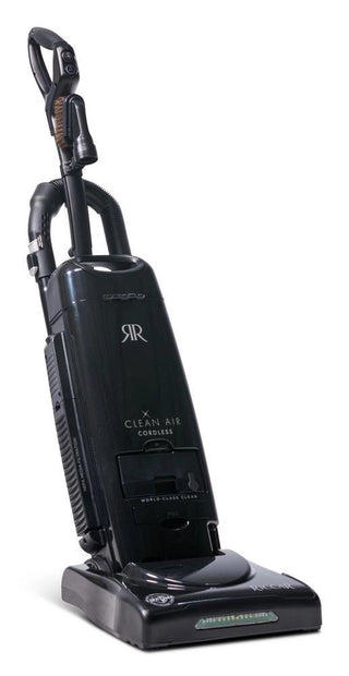 The Riccar R27CV Cordless Upright Vacuum by Imagine Sewing & Vacuum is a black model with a handle, hose attachment, and "Clean Air Cordless" label, offering powerful cleaning and advanced HEPA filtration. Shown on a white background.