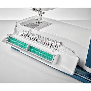 Close-up of a Husqvarna Viking Designer Sapphire 85 sewing and embroidery machine by Husqvarna Viking, with its accessory compartment open to display several green bobbins neatly stored inside.