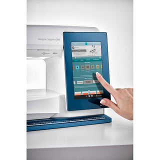 A hand interacts with the Husqvarna Viking Designer Sapphire 85’s digital screen, browsing design options via its mySewnet connectivity.