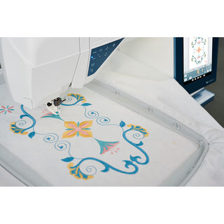 A Husqvarna Viking Designer Sapphire 85 sewing and embroidery machine stitches a colorful floral and swirl pattern on white fabric, with the design shown on a screen enhanced by the intuitive JoyOS ADVISOR.