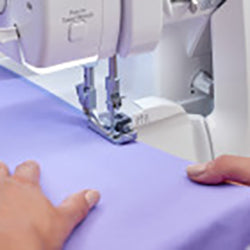 A person using a Baby Lock Acclaim Serger sewing machine to sew a piece of fabric.