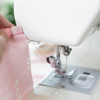 A person is sewing a pink fabric on a Baby Lock Joy Sewing Machine.