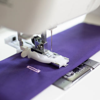 A Baby Lock Zeal Sewing Machine is being used to sew a purple fabric.