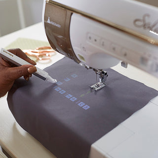 A person is using a Baby Lock Solaris Vision Sewing and Embroidery Machine to sew a piece of fabric.