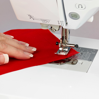 A woman's hand sewing a red piece of fabric on a Baby Lock Soprano Sewing and Quilting Machine.