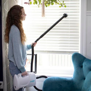 A woman holding a Simplicity S100 Sport Portable Canister Vacuum in front of a window.