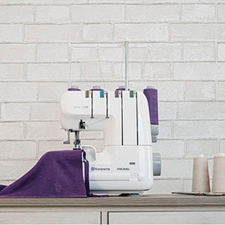 A Husqvarna Viking sewing machine sits on a table with purple fabric.