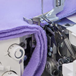 A purple fabric is being sewn on a Baby Lock Acclaim Serger sewing machine.