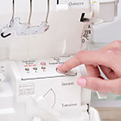 A person using a Baby Lock Accolade Serger sewing machine with a button on it.