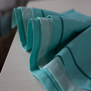 A pair of Baby Lock teal colored napkins on a table.