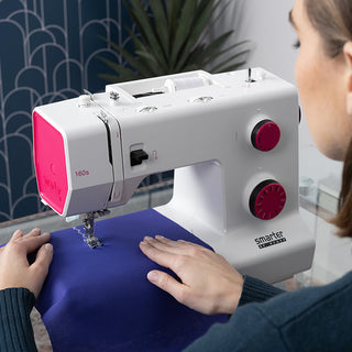 A woman is sewing a piece of fabric on a Smarter by Pfaff 160s sewing machine manufactured by PFAFF.